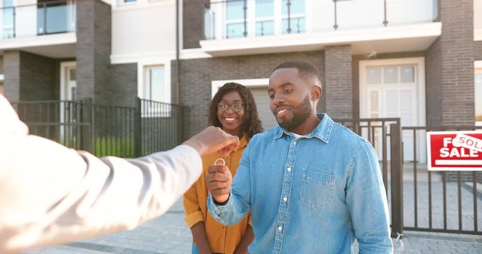 Rear of real-estate selling house to African American happy couple and handing keys. Outdoor. Joyful married man and woman hugging and buying home at outskirt. Getting dwelling in suburb. back view.