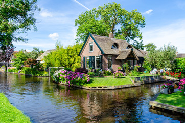 Fototapeta na wymiar Giethoorn, Netherlands: Landscape view of famous Giethoorn village with canals and rustic thatched roof houses. The beautiful houses and gardening city is know as 
