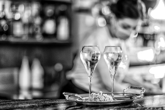 Female Bar Tender Wearing Face Mask Preparing Two Glasses Of White Wine , Selective Focus, Bokeh.