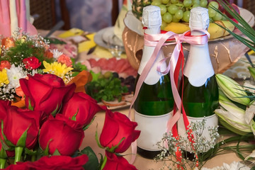 Two bottles of champagne tied with a ribbon in the middle of bouquets of flowers, indicating a wedding party or other festive feast
