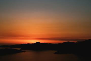 Orange sunset sky. The sun sets behind the silhouette of the mountain.