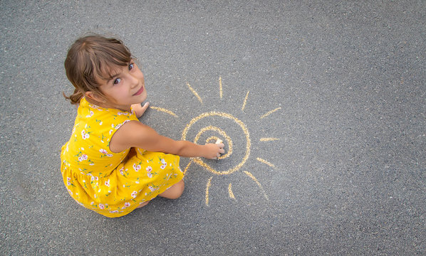 The child draws the sun on the asphalt. Selective focus.