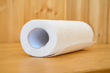 Roll of paper towels on a wooden table against a background of wooden walls. Everyday hygiene items in the kitchen. Ecological materials for cleaning and hygiene.