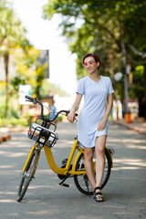 young woman with pink hair walks in the park with a bike eating ice cream in the summer. Environmental mode of transport