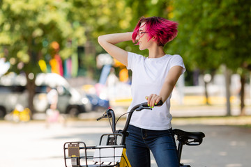 young woman with pink hair walks in the park with a bike eating ice cream in the summer. Environmental mode of transport