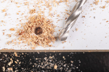 Making holes with a metal drill in a chipboard. Minor jobs in the carpentry workshop.