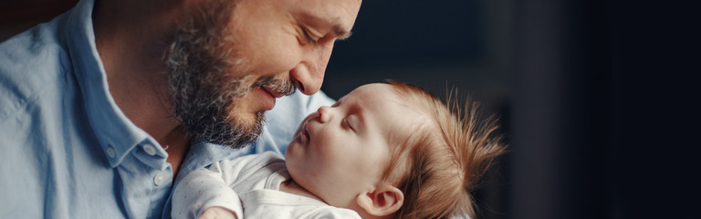 Closeup of middle age bearded Caucasian father with newborn baby. Smiling proud man parent holding a child. Authentic lifestyle touching tender moment. Single dad family life. Web banner header. - 372772394