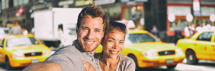 New York selfie couple taking photo on NYC city summer holiday vacation travel with yellow taxi cabs panoramic background. Man and woman tourists happy smiling.