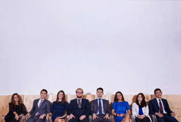 Portrait of a young confident workers dressed in corporate clothes sitting in hall before conference, multi ethnic group of successful entrepreneurs in formal wear waiting for start business meeting