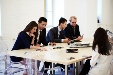 Multi ethnic group of confident business people talking among themselves while waiting for beginning of the conference creaive architects in formal wear using mobile phones during work break in office