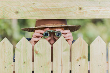 Curious neighbor stands behind a fence and watches with binoculars