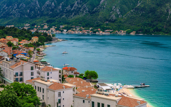 Aerial scenic view of residential buildings along the coast of Kotor Bay and mountains in the background in the summer in Dobrota, Montenegro