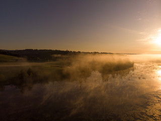 Morning on the lake in the forest with fog or steam on the background of the sun