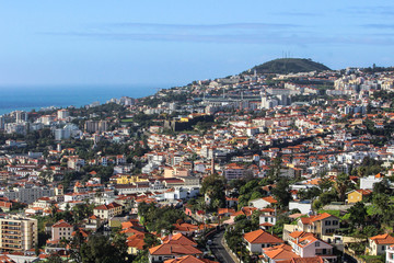 Fototapeta premium Aerial view of Funchal,the capital of Madeira Island,Portugal,on the coast of Atlantic Ocean. One of Portuguese main tourist attractions.Seafront houses with red roofs,mountain valley and sea.
