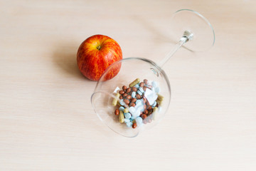 Pills in a glass bowl and red apple on a beige background. Rich in vitamins.