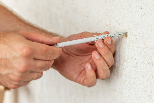 Worker inserts plastic wall plug into a hole. Close up.