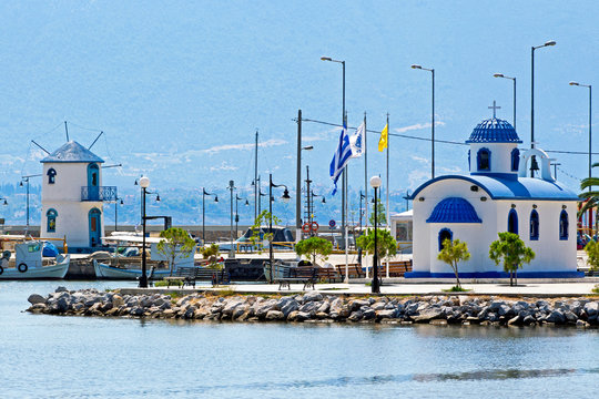The chapel of Saint Nikolaos in the port of Nea Artaki  in Euboea/ Greece and a windmill with the same colours  in the backround.  Sunny summer day
