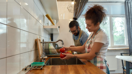 Happy young couple washing vegetables, tomatoes in the kitchen while preparing ingredients for dinner. Cooking at home concept