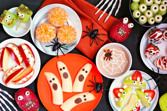Healthy Halloween fruit snacks. Assorted fun, spooky treats. Top view table scene over a black stone background.
