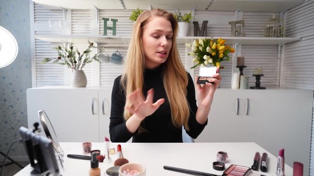 Beauty blogger woman filming daily makeup routine tutorial on camera. Influencer blonde lady live streaming eye shadow palette review in home studio with professional lighting equipment. Vlogger job.