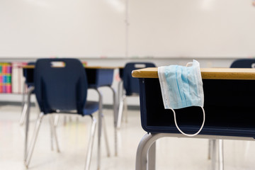 Protective surgical mask resting on top of a student desk within a clean contemporary classroom