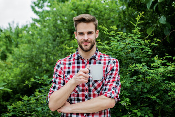 Naklejka na ściany i meble good morning. fresh inspiration and energetic beverage. handsome bearded guy drinking tea outdoor. he loves cocoa. food and drink. cheerful man in checkered shirt drink morning coffee