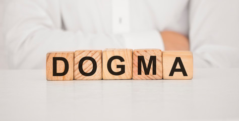 Close up young man's hand in white shirt wooden block cube for Dogma wording on white marble table floor