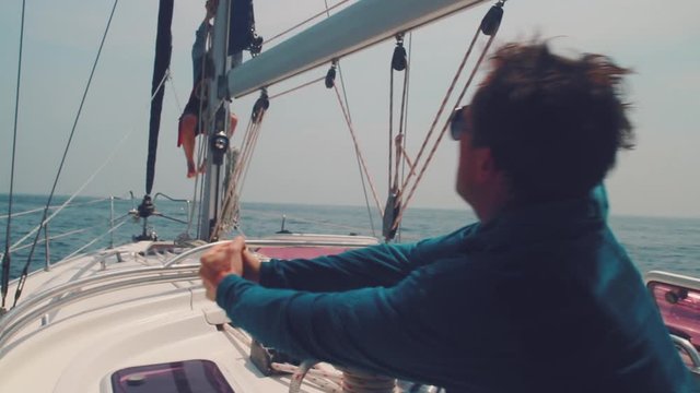 Men on the boat. Man works with winch on the sailing boat and hoists his buddy to the top of the mast