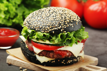 A black burger with vegetables and beef meat