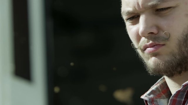 Close up of man face with beard and hussar moustache looking concentrated. Video. Brutal male face during work process with flying wooden dust.