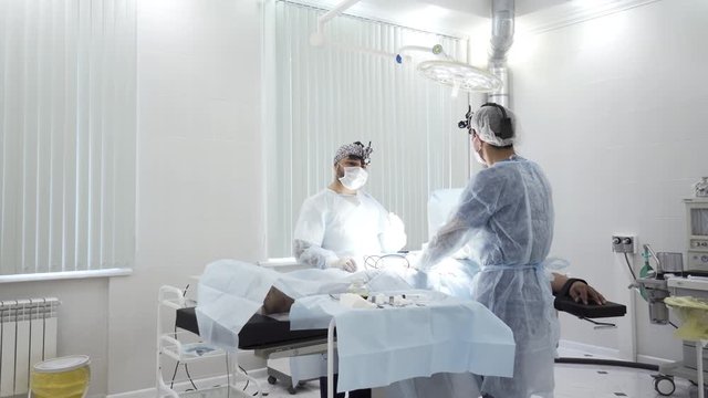 Two male surgeons at the work with time lapse effect. Action. Sedated patient lying on the table during surgical procedure inside the hospital room.