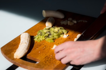 Woman's hands cutting fresh banana on the wooden board on the kitchen