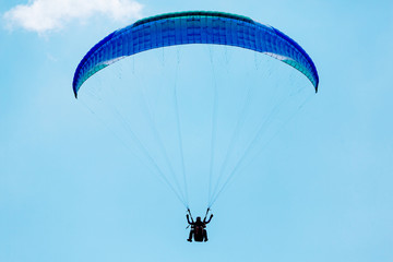 Blue Paraglider flying into the sky with clouds on a sunny day