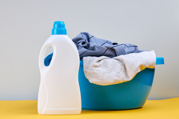 detergent bottle with stack of a colored clothes for laundry cleaning and washing service. background backdrop. copy space. studio shoot. laundry concept