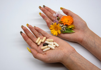 Two female hands on a light background. In one hand, capsules and tablets, in the other medicinal...