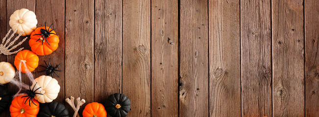 Halloween corner border banner of orange, black and white pumpkins, bones and spiders against a rustic wood background. Copy space.