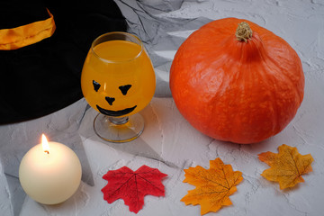 Halloween composition with drink, orange cocktail, pumpkin, candle, hat and fallen leaves on textured background