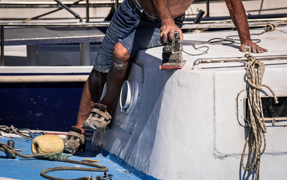 the old man is sanding the paint of his boat, doing maintenance, closeup.