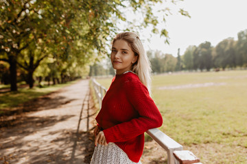 Glorious blonde woman standing relaxed in the park. Lovely girl enjoying nice autumn view.