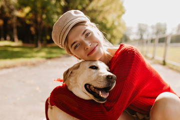 Charming girl and her dog having good time in the autumn park. Lovely blonde with beautiful dog posing on the camera.