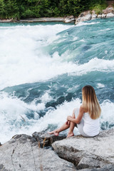 A girl sits near a mountain river in Bavaria, Germany. A beautiful stormy river. Tourism in Bavaria. Tourist place in Europe. Relax in nature. Rest in the mountains. Rest near the mountain river.