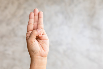 Hand showing three finger symbol on grey background with copy space