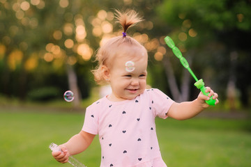 little girl blows bubbles in the park on green grass
