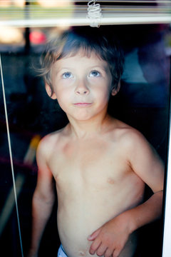 Little cute boy throught window making funny faces, home alone lifestyle concept