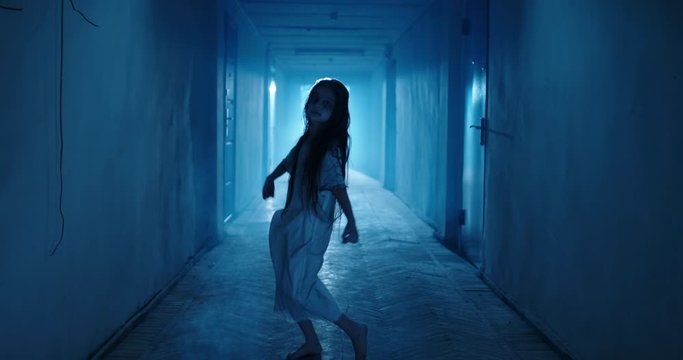 Little girl in white dress looking like a ghost carelessly dancing in the hallway of a haunted house - halloween costume party, horror movie 4k footage