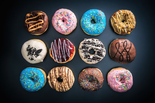 Top down view of various colorful donuts, on top of black background.