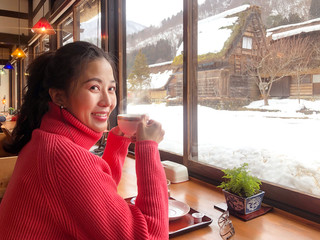 Woman tourist drinking coffee in the morning  and enjoying the winter snow view at Shirakawago village, Gifu, Japan.
