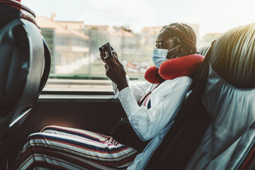 Side view of a young black woman with braids and in a virus protective mask sitting on the seat...