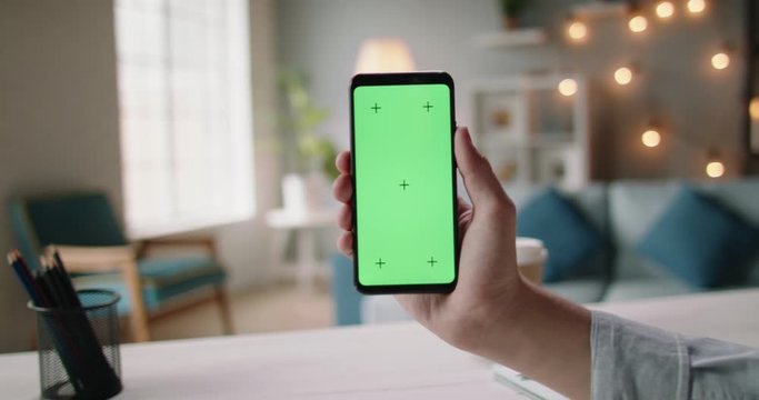 Close up shot of hand of guy holding a smartphone in cozy living room. A green screen mock up chroma key template 4k footage