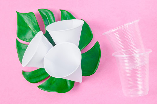 Disposable paper cone water cups and plastic water cups with green leaf on pink background.